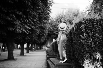 Portrait of a fabulous young woman in striped overall walking on the barrier in the park. Black and white photo.