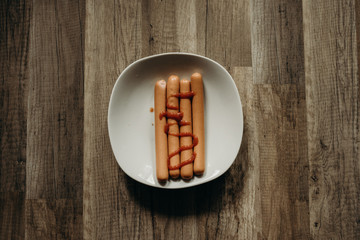 Delicious sausages with ketchup on a white plate on the kitchen.