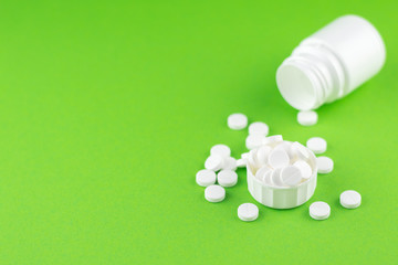 Close up white pill bottle with spilled out pills and capsules in cap on green background with copy space. Focus on foreground, soft bokeh. Pharmacy drugstore concept