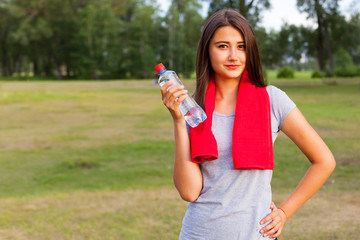 Beautiful teenage girl with a bottle of water, against a green summer park.