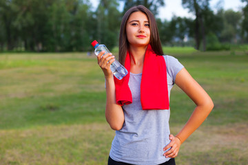 Beautiful teenage girl with a bottle of water, against a green summer park.