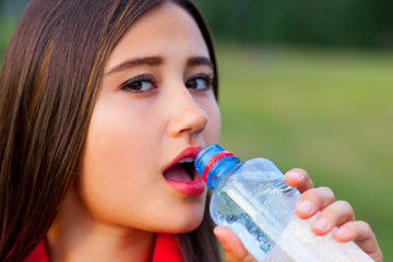 Beautiful teenage girl with a bottle of water, against a green summer park.