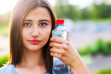 Beautiful teenage girl with a bottle of water, against a green summer park.