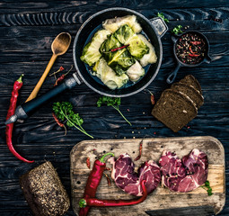 Traditional ukrainian meal called golubtsi on dark background with raw slices of meat on the wooden board, rye bread, chilly paper and other spicies. Top view.