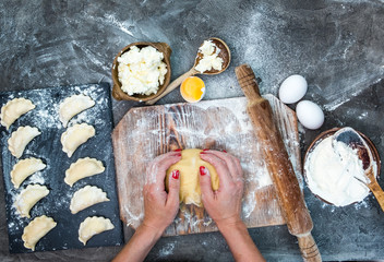 Female hands kneading raw dough on wooden board. Flowered dark table with varenyky, eggs and rolling pin. Top view, view from above.