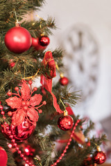 Part of a beautiful Christmas tree with balls and ornaments against a blurry big clock