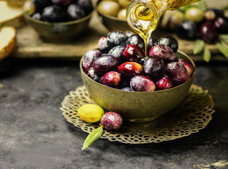 Bottle pouring organic olive oil in a bowl of fresh olives. Close up view with copy space