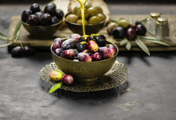 Virgin olive oil pouring in bowl of fresh olives. Close up view with copy space.