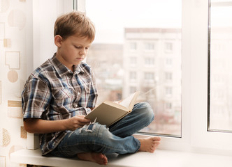 boy reading a book sitting on the windowsill