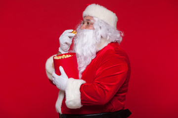 Traditional Santa Claus watching TV, eating popcorn. Christmas. Red background. emotions fear surprise