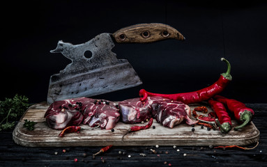 Two slices of raw meat on wooden board with old butcher chopping knife and some chilly paper
