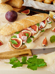 Sandwich with hamon, figs, arugula and Parmesan cheese. Baked products and ingredients in the background.