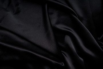 Dark black silky, satin  fabric, wave, draperies. Beautiful textile backdrop. Close-up. Top view 