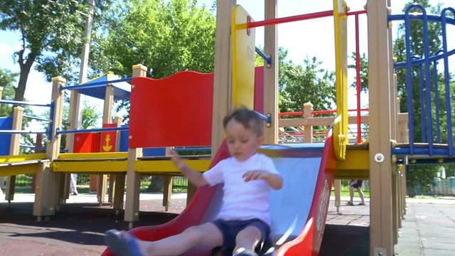 A child with a great pleasure rides a slide on a playground in a slow pace