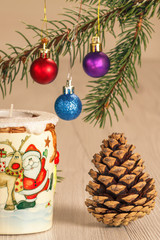 Burning candle and natural fir tree branches with Christmas ornament on grey wooden boards