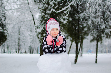 Fototapeta na wymiar A little girl sitting on snow in winter park