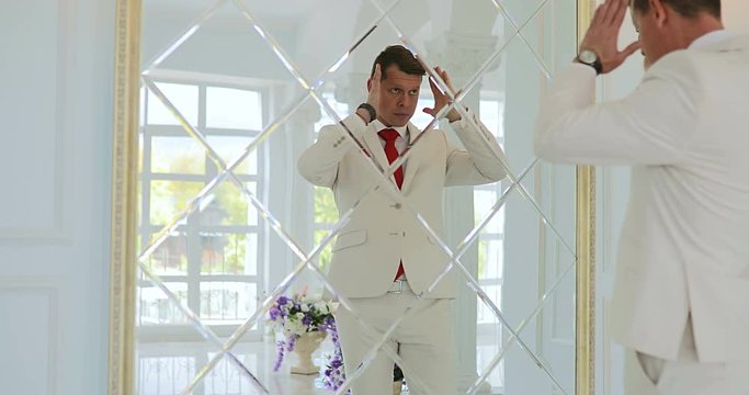groom looks in the mirror / businessman looks at his reflection in the mirror