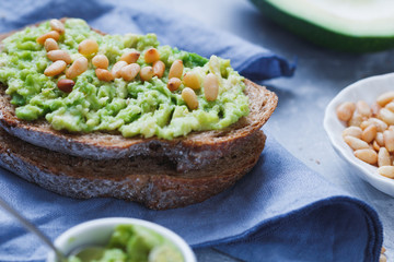 Close-up of the rye bread sandwich with smeared avocado with fried pine nuts on the textured blue background. The concept of health and fitness eating.