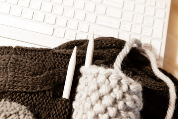 Gray knitted sweater. Handmade knitting. Big wool yarn ball and needles, white keyboard. Flat lay...