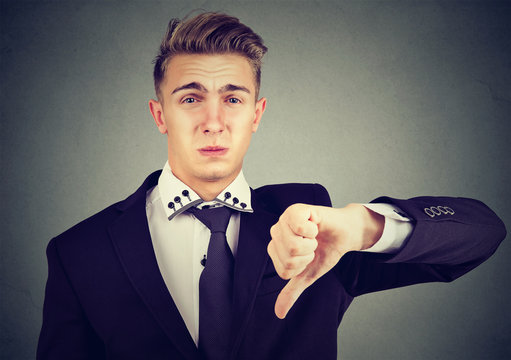Angry disappointed young business man showing thumbs down sign, in disapproval isolated on gray background. Negative emotion facial expression feelings