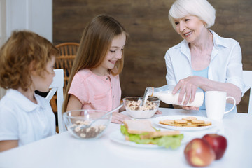 Caring granny. Kind friendly loving granny pouring milk into a bowl of her granddaughter