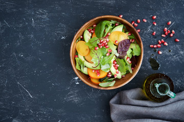 Seasonal salad. Persimmon, avocado, pomegranate and different lettuce leaves in wooden bowl
