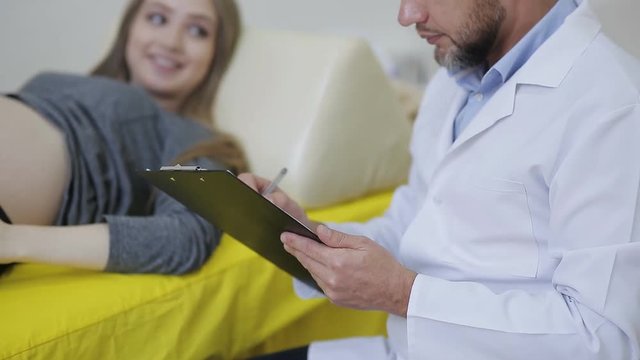 A pregnant woman attending an experienced gynecologist. The doctor writes to the medical chart the readings of the pregnant woman
