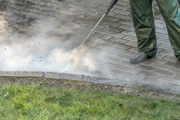 Worker cleaning driveway with high pressure water jet, high pressure cleaner. High pressure deep cleaning. 