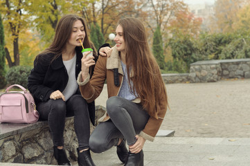 Two girlfriends try to warm up with a hot drink in the outdoors