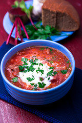Ukrainian traditional borsch. Russian vegetarian red soup  in blue bowl on red wooden background.  Borscht, borshch with beet. Close up.