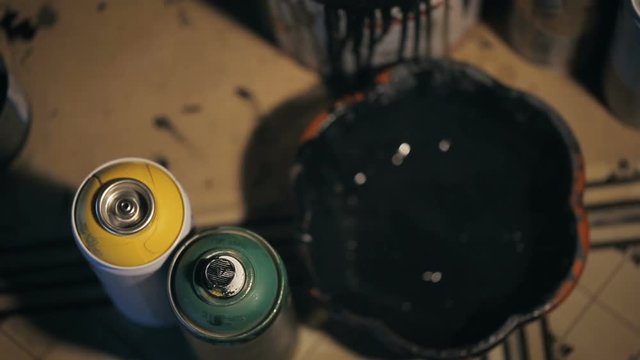Shot of Painter who pours the solvent into the bowl with black paint and mixing it by brush. Action takes place in the artist's studio.