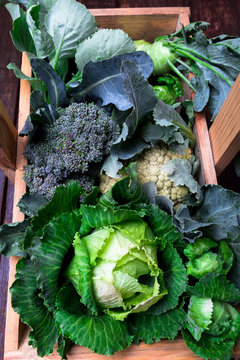 Variety of cabbages in wooden basket on brown background. Harvest. Top view.