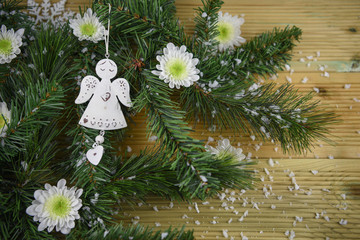 Christmas photography image of green tree branches and white winter flowers laid on wood table with angel and heart decoration all sprinkled in snow