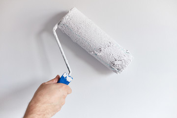 Male hand painting wall with paint roller. Painting apartment, renovating with white color paint
