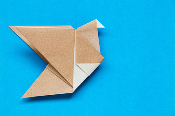Brown origami paper in flying bird shape on blue background