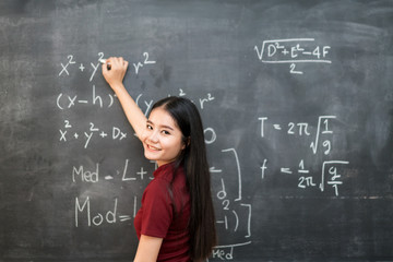 Beautiful Asian student writing on blackboard with chalk in classroom.