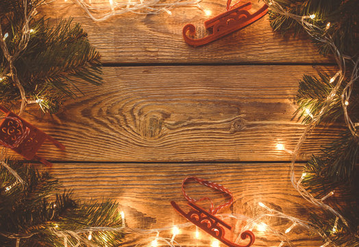 Image on top of wooden table with burning garland, spruce branches, Christmas toys.