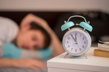 Wecker auf Nachttisch, schlafender junger Mann, entspannt 