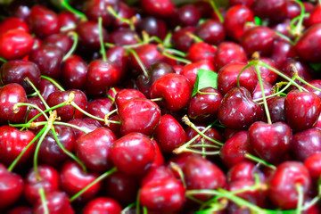 Close up of pile of ripe cherries with stalks and leaves. Large collection of fresh red cherries. Ripe cherries background.