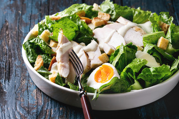 Classic Caesar salad with grilled chicken breast and half of egg in white ceramic plate. Over old dark blue wooden background. Close up. Rustic style