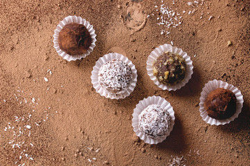 Variety of homemade dark chocolate truffles with cocoa powder, coconut, walnuts over cocoa powder as background. Top view, copy space.