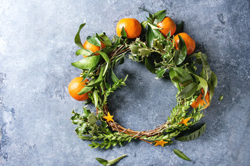 Christmas wreath with clementines tangerines and green branches over blue texture background. Top...