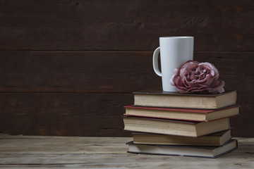 Composition on a wooden background. Rose bud, books and a white cup
