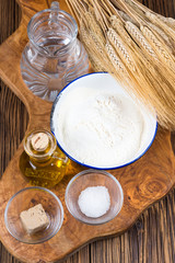 Frische Zutaten für einen traditionellen Pizzateig auf einem Brett aus Olivenholz mit Getreideähren im Hintergrund