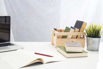 The office tool for work ,laptop,paper work, bookd and pen ,they are put beside tree pot on office desk,white sartin curtain background.top, mobile phone,paper work, pen ,they are put on office desk,