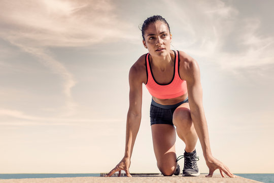 Young woman on sea wall, in start position, preparing for run