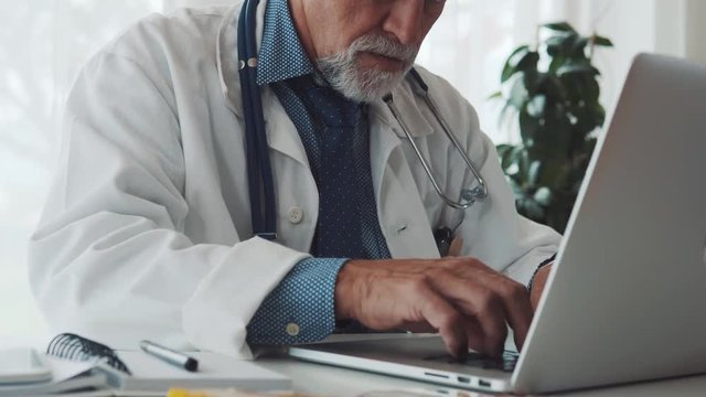 Senior doctor with laptop working at the office desk.