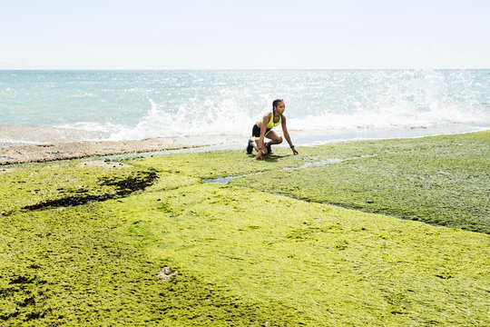 Young woman beside sea, in start positions, preparing for run