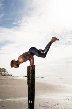 Young man training, doing handstand with raised legs on wooden beach posts