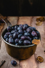 fresh plums in old metal pot on brown gradient background with dry leaves